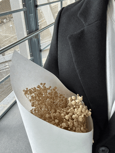 a person holding a bouquet of baby 's breath flowers in front of a window