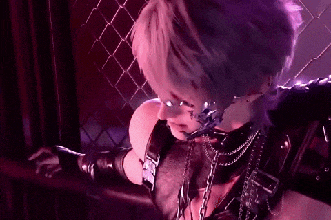 a woman with purple hair and a chain around her neck is standing in front of a chain link fence in a dark room .