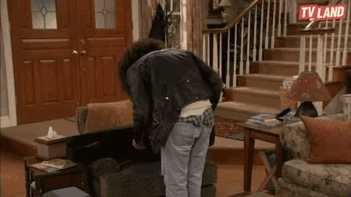 a man in a leather jacket is standing in a living room with stairs and a tv land logo in the background