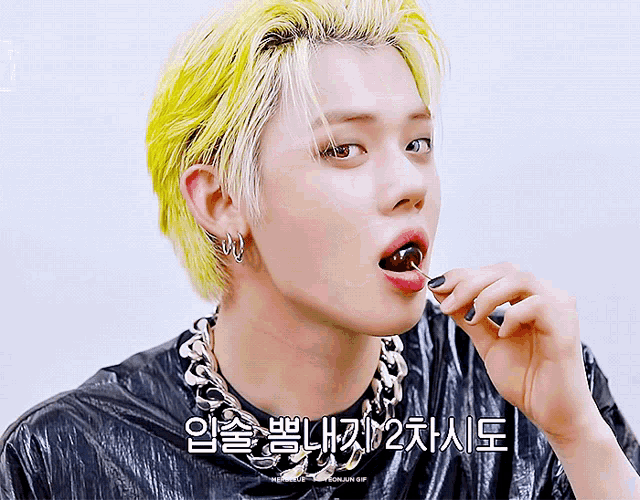 a man with yellow hair is eating a lollipop with korean writing on the bottom