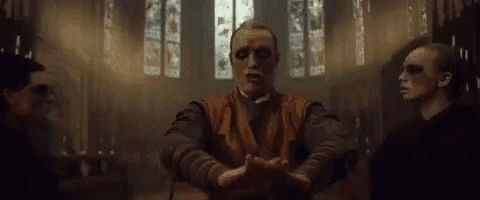 a man with a mask on his face is standing in a church with his hands in the air .