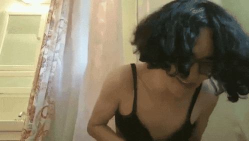 a woman in a black bra stands in a bathroom next to a shower curtain