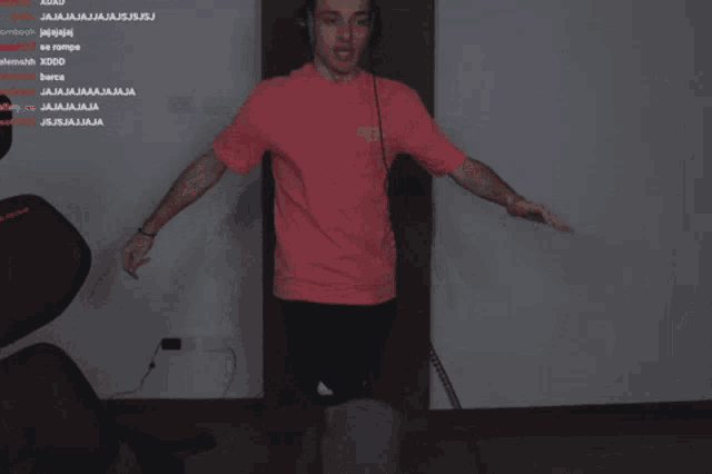 a man wearing headphones and a pink shirt stands in front of a wall with a bunch of spanish text on it