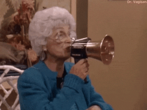 an elderly woman is blowing into a megaphone while wearing glasses .