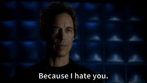 a man in a black shirt is standing in front of a blue wall and saying because i hate you .