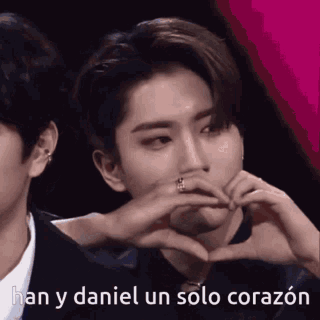 a man is making a heart shape with his hands while another man watches .