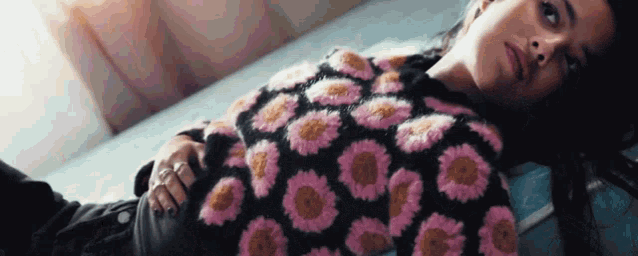 a woman in a sweater with flowers on it is laying on a bed .