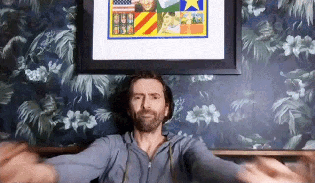 a man with his arms outstretched is sitting in front of a framed picture