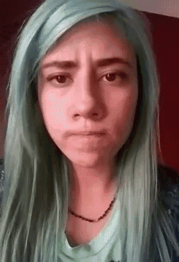 a woman with long green hair is making a funny face .
