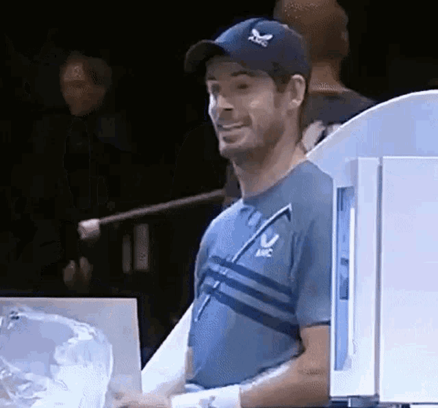 a man wearing a baseball cap and a blue shirt is smiling while holding a glass .