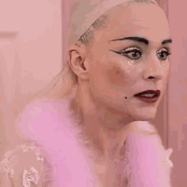 a woman with a wig on her head is wearing a pink fur coat and making a funny face .