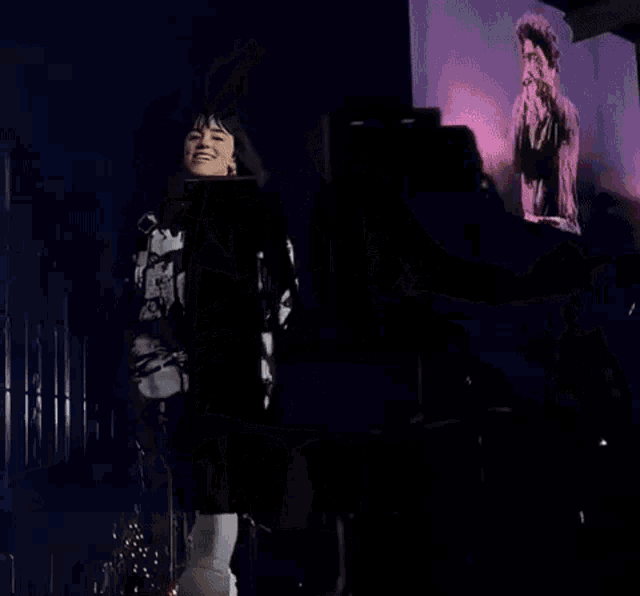 a woman is standing on a stage holding a microphone and pointing at something .