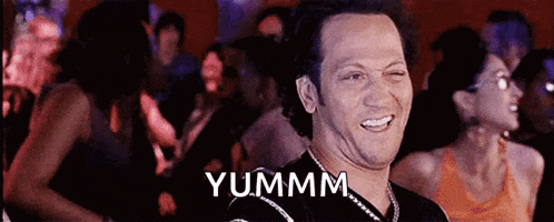 a man is making a funny face in front of a crowd and the word yummm is above him .