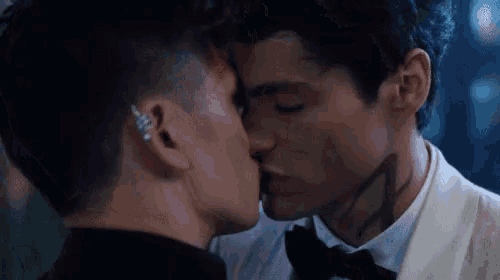 a man in a tuxedo kisses another man in a black bow tie