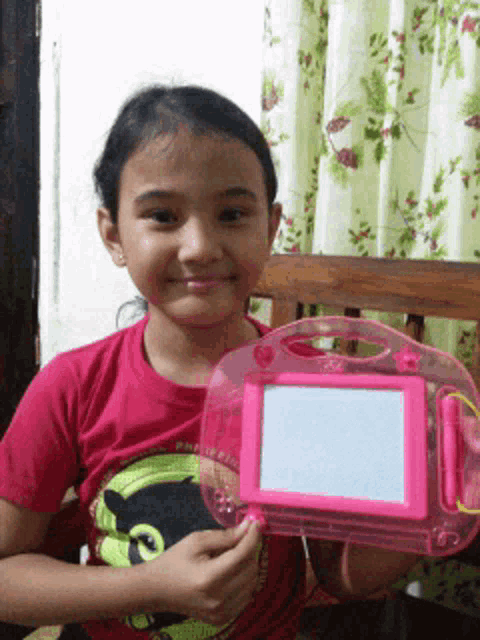 a little girl in a pink shirt is holding a pink drawing board