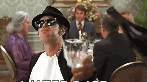 a man wearing a hat and sunglasses is holding a glass of wine while sitting at a table .