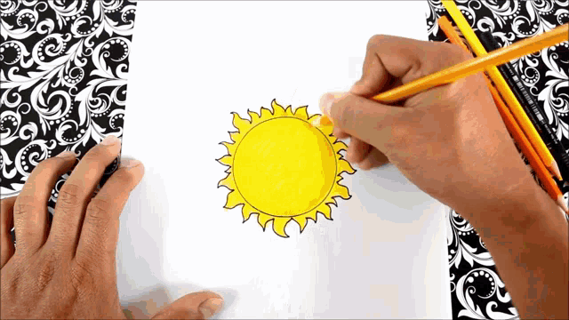 a person is drawing a sun with a pencil on a piece of paper