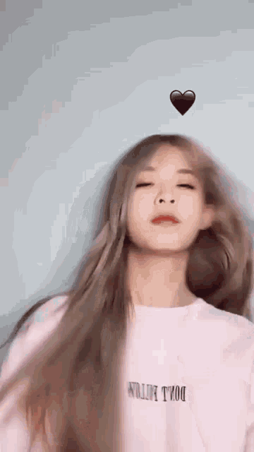 a woman with long hair is wearing a pink shirt and a heart is floating above her head .