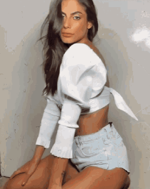 a woman wearing a white crop top and denim shorts
