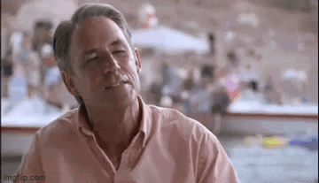 a man in a pink shirt is sitting at a table in front of a crowd .