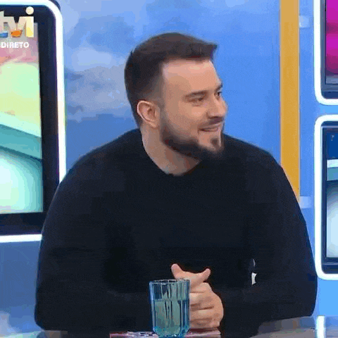 a man with a beard is sitting at a table with a glass of water and smiling .