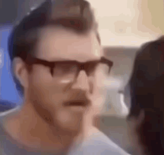 a man wearing glasses is talking to a woman in a blurry video .