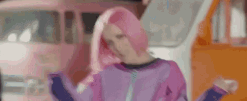 a woman with pink hair is dancing in front of a pink bus .