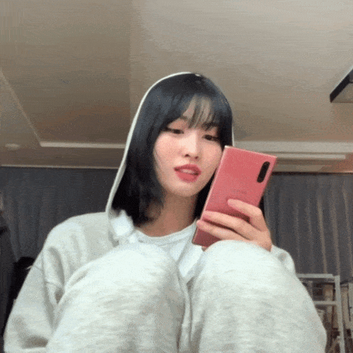 a woman in a hoodie is holding a pink samsung phone