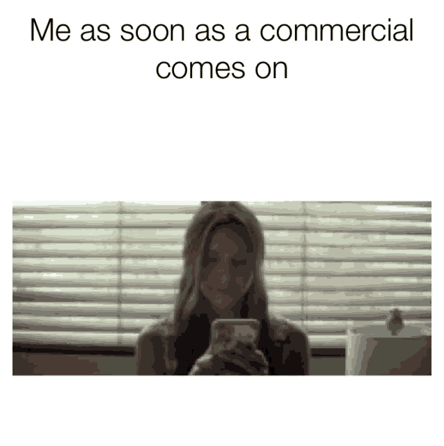 a woman is sitting in front of a window looking at her phone with the caption me as soon as a commercial comes on