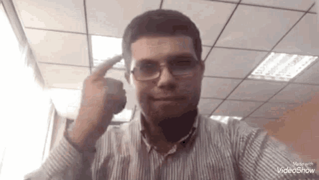 a man wearing glasses and a striped shirt is pointing his finger at the camera .