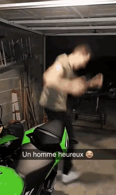 a man is standing on a green motorcycle in a garage with a caption that says " un homme heureux "