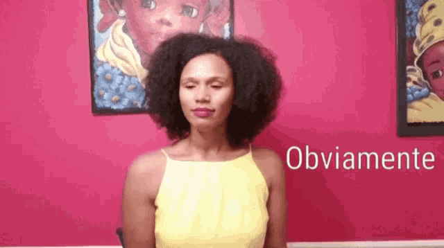 a woman in a yellow top is standing in front of a pink wall and making a face .