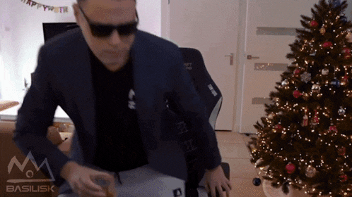 a man in a suit and sunglasses is standing in front of a christmas tree and a sign that says basilisk