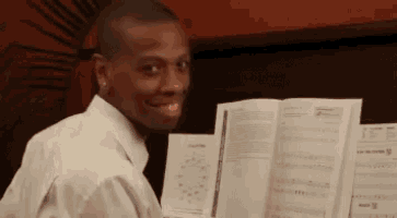 a man in a white shirt is smiling while holding a book of sheet music