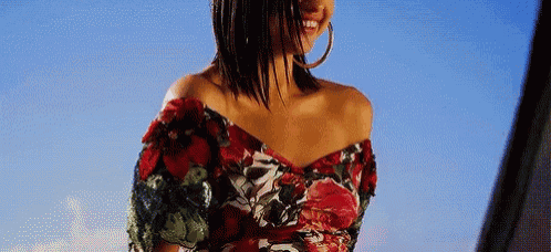 a woman wearing a floral off the shoulder top and hoop earrings .