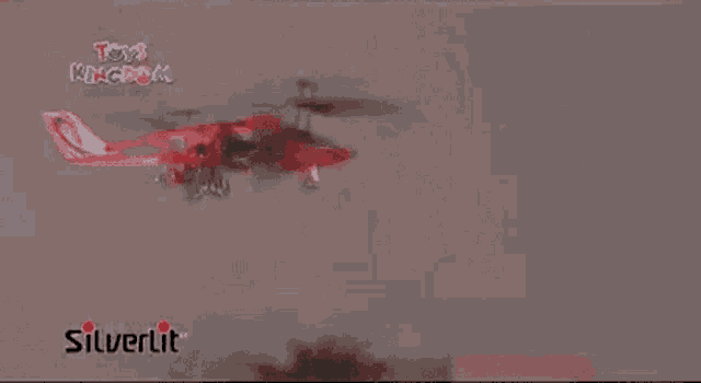 a red and white airplane is flying in the air with a silverlit logo in the corner