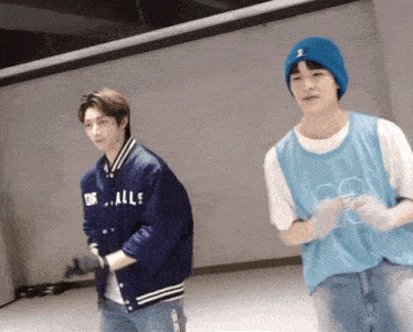 a man wearing a blue jacket that says dr. alls stands next to another man wearing a blue beanie