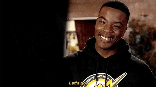 a young man in a black hoodie is smiling and talking to someone .