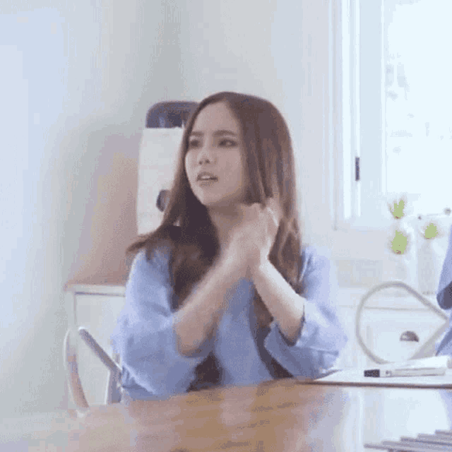 a woman in a blue shirt is sitting at a table with her hands on her face .