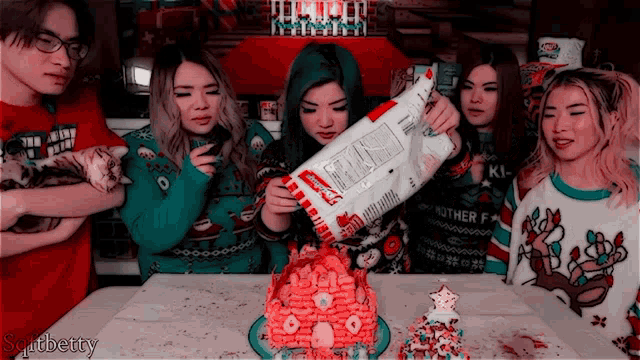 a group of people are gathered around a gingerbread house and one of the girls is holding a bag of kraft macaroni and cheese