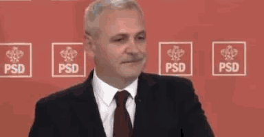 a man in a suit and tie is standing in front of a red wall .