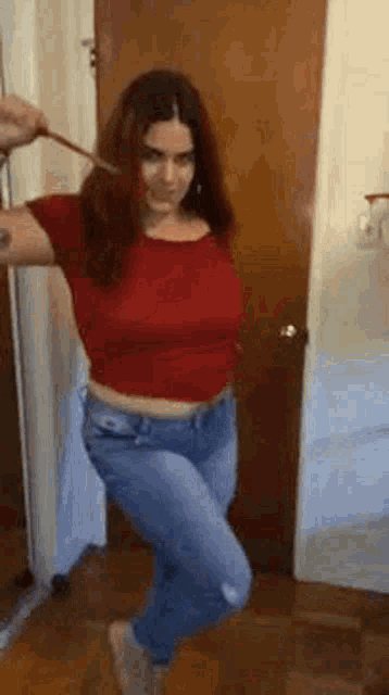a woman in a red top and jeans is standing in front of a door .