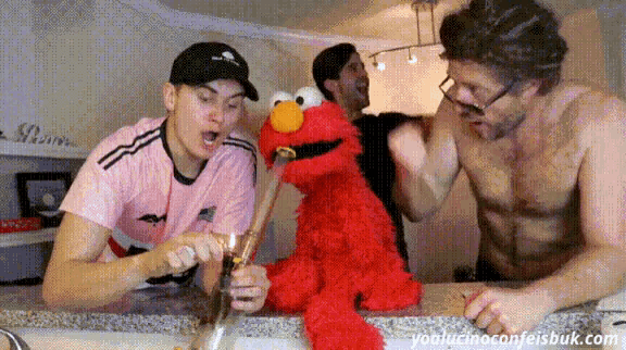 three men are playing with elmo the sesame street mascot on a kitchen counter