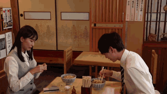 a man and woman sit at a table with bowls of food