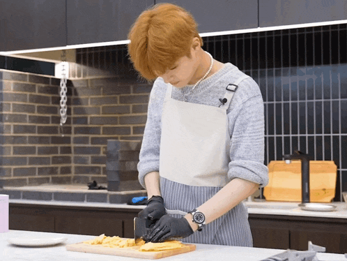 a man wearing an apron and black gloves is cutting food on a wooden cutting board