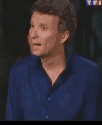 a man in a blue shirt is making a funny face while talking .