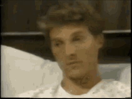 a man in a hospital gown is laying in a hospital bed and looking at the camera .