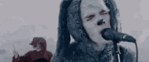 a man in a wolf costume is singing into a microphone while another man looks on .