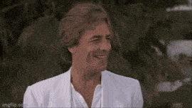 a man in a white suit and tie is driving a blue convertible car .