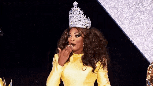 a woman wearing a yellow dress and a tiara is blowing a kiss .